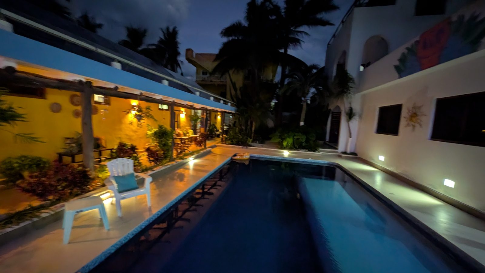 The pool lit at dusk, with palms and warm yellow walls