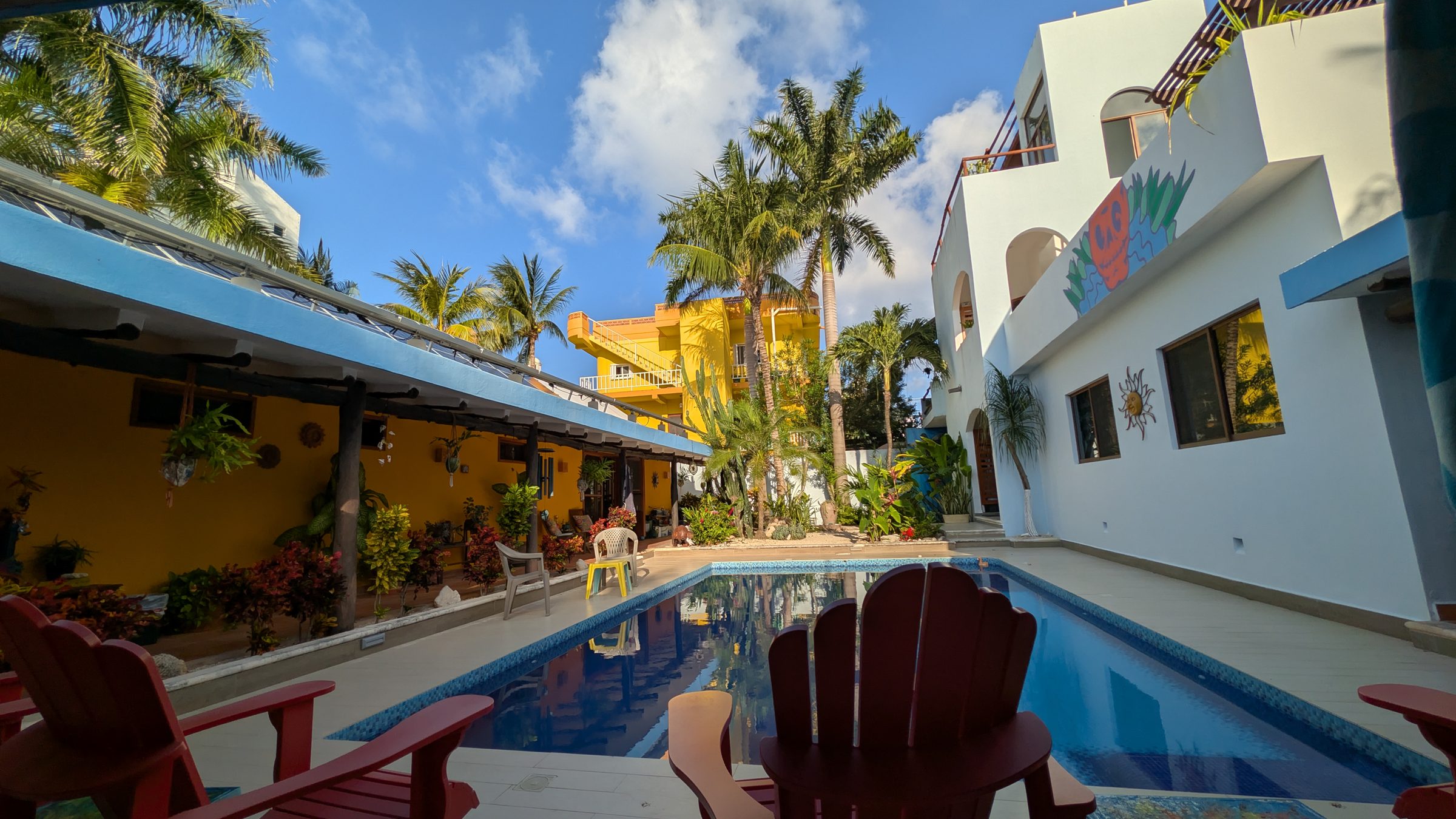 The pool and courtyard at Casa Agua Azul under a blue sky, framed by palms and white walls
